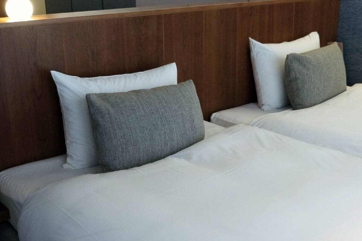 Quarto de hotel com duas camas, cada uma com roupa de cama branca e almofadas cinzentas.