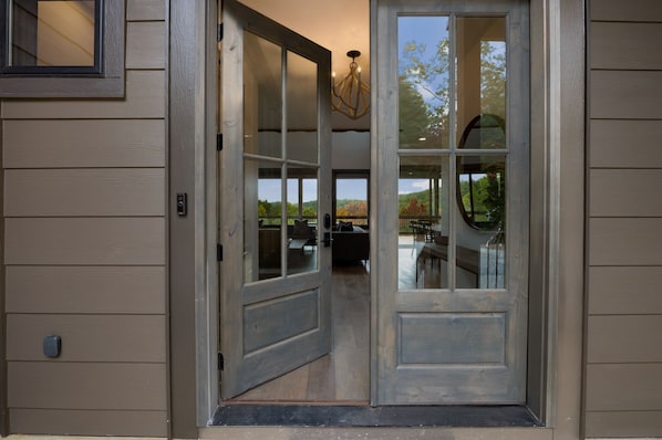 A wooden door with glass panels, a visible doormat, and a chandelier. - Vacay Chalet- Blue Ridge GA (Blue Ridge)