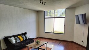 A living room with a black sofa, a wooden coffee table, and a large window with a view of greenery.