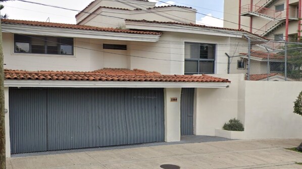 A two-story building with a tiled roof, a closed garage door, and a small garden area.