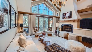 A spacious living room with a fireplace, large windows, and a high ceiling.