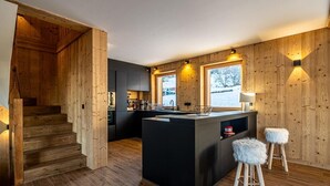 A modern kitchen with wooden accents, a central island, bar stools, and a view of the outdoors.