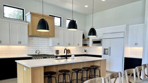Une cuisine moderne avec des meubles blancs, un îlot central doté de tabourets et un éclairage suspendu.
