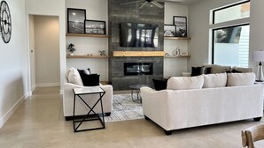 Un salon moderne comprenant un canapé, un fauteuil et une table basse, une cheminée et un téléviseur fixé au mur.