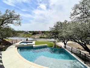 A swimming pool with a curved edge, surrounded by a black metal fence and a grassy area.