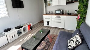 Un espacio habitable moderno con sofá, mesa de centro y zona de cocina con armarios y televisor.