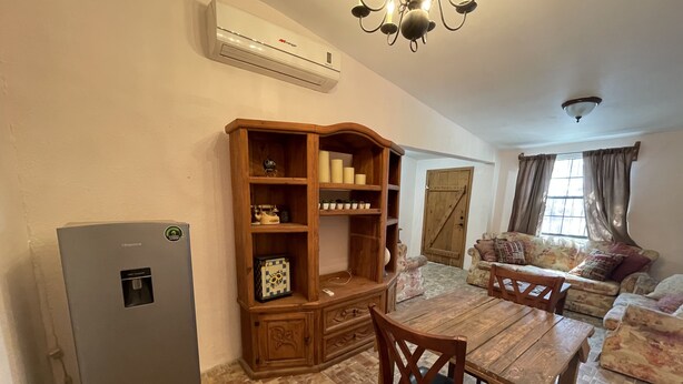 A living room with a wooden cabinet, a dining table with chairs, a sofa, and a refrigerator.