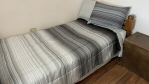 A small, neatly made bed with a striped bedspread and two pillows, a wooden nightstand, and a wall socket.