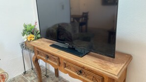 A flat-screen TV on a wooden TV stand with a small shelf below.