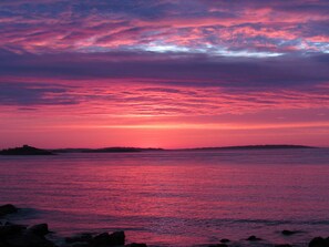 A sunset over a calm sea with a distant landmass silhouetted against the sky.