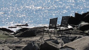 A rocky beach with two chairs facing the ocean, under clear skies.