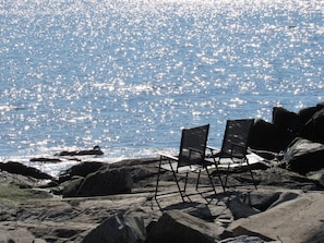 A rocky beach with two chairs facing the ocean, under clear skies.