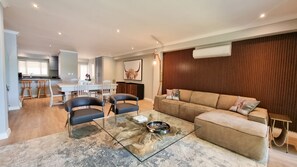 A modern living room with a glass coffee table, a sofa, and a dining area with a kitchen in the background. - Pearl Valley Golf Lodge - loadshedding free (Pearl Valley Golf Estate and Spa)