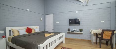 A bedroom with a bed, a desk, a chair, a TV, and a small shelf with a plant and shoes.