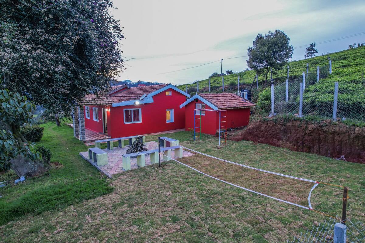 A red house with a tiled roof, a small garden, and a fenced area.