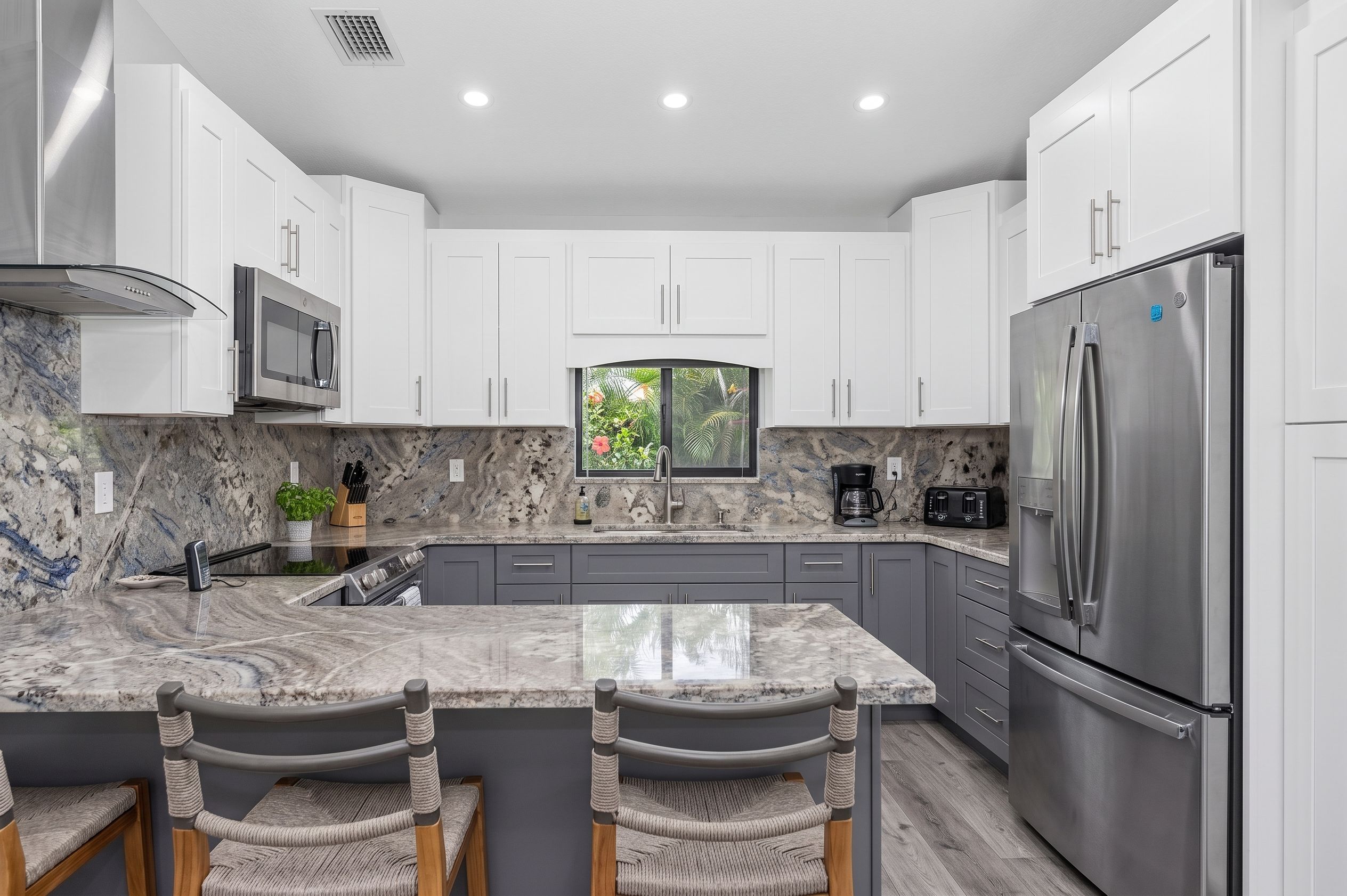 A modern kitchen with white cabinets, a stainless steel refrigerator, a built-in oven, and a marble countertop.