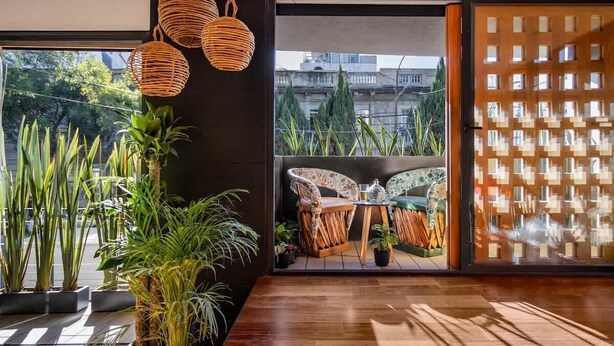 Una habitación moderna con un amplio ventanal, suelo de madera, lámparas colgantes de mimbre y vistas a la ciudad.