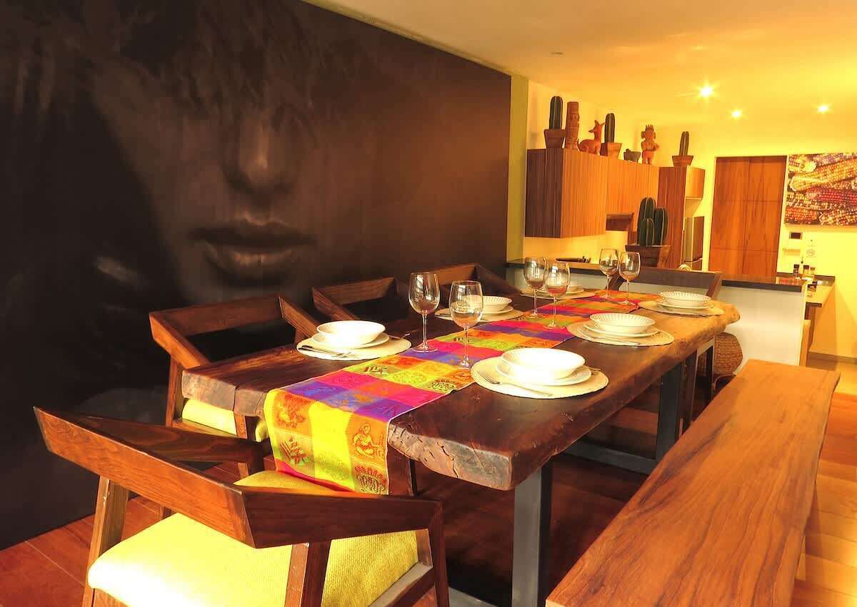 Un coin repas avec une longue table en bois, dressée pour quatre personnes, agrémentée d’un chemin de table coloré et d’assiettes blanches.