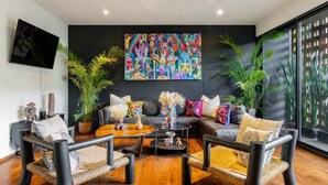 Una sala de estar moderna con un sofá de cuero negro, dos sillones negros, una mesa de centro y un cuadro abstracto de colores en la pared.