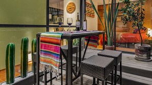 Un área de comedor al aire libre con una mesa cubierta con un mantel colorido, dos sillas de mimbre y una planta de cactus.