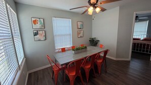 A dining area with a wooden table, red chairs, a ceiling fan, and artwork on the walls.