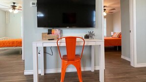 A modern living room with a flat-screen TV mounted on the wall, a white desk, and an orange chair.