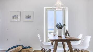 Un comedor con una mesa de madera, sillas blancas, una cesta tejida y una lámpara colgante.