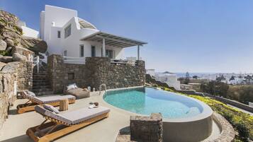 Una villa moderna con piscina infinita privada, paredes de piedra y vistas a la ciudad.