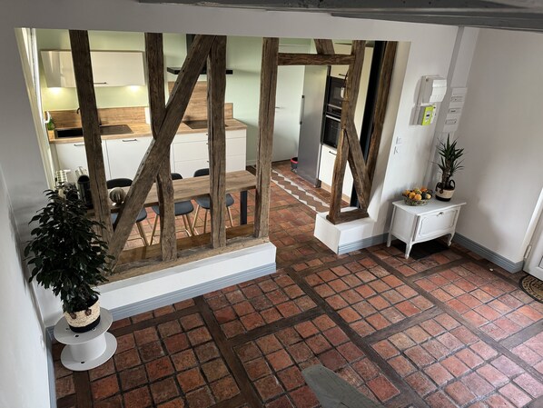 A room with a rustic wooden beam structure, a dining table with chairs, a white cabinet, and a potted plant.
