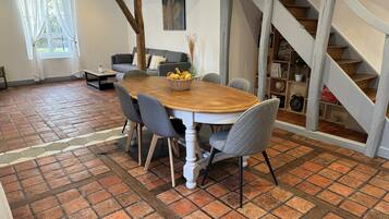 Ein Essbereich mit einem Holztisch, grau gepolsterten Stühlen, einem Boden mit Backsteinmuster, einer Treppe und einem Bücherregal mit Büchern und Dekorationsobjekten.
