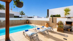 A pool area with lounge chairs, a barbecue grill, and potted plants.