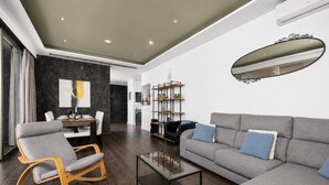 A modern living room with a grey sofa, a rocking chair, a glass coffee table, and a bookshelf.