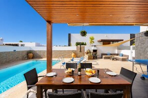An outdoor dining area with a pool, wooden pergola, and stone walls. - Villa Sal Marina - Three Bedroom Villa, Sleeps 6 (Puerto del Carmen)