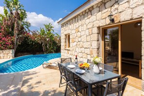 A stone house with a pool, outdoor dining area, and lush vegetation.