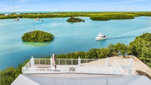 Vista costeira com barcos na água, um corrimão branco e vegetação.