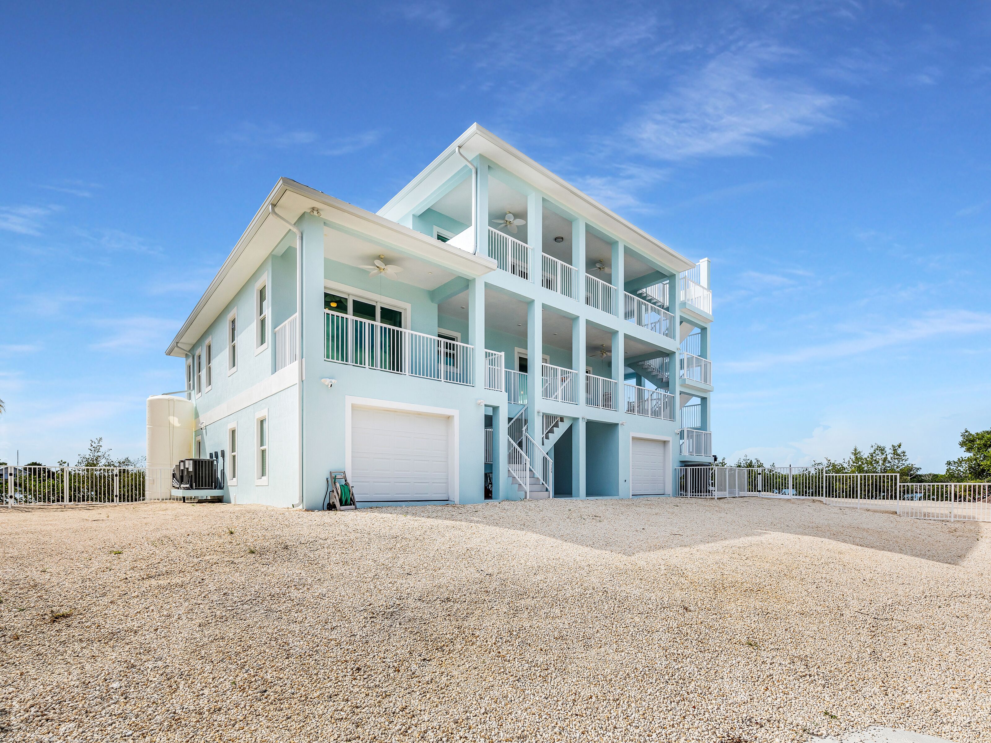 Une propriété en bord de mer, composée de plusieurs étages, dotée de balcons, d’un garage et d’une allée gravillonnée.