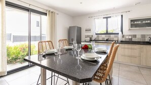A modern kitchen with a dining area, large windows, and a view of greenery outside.