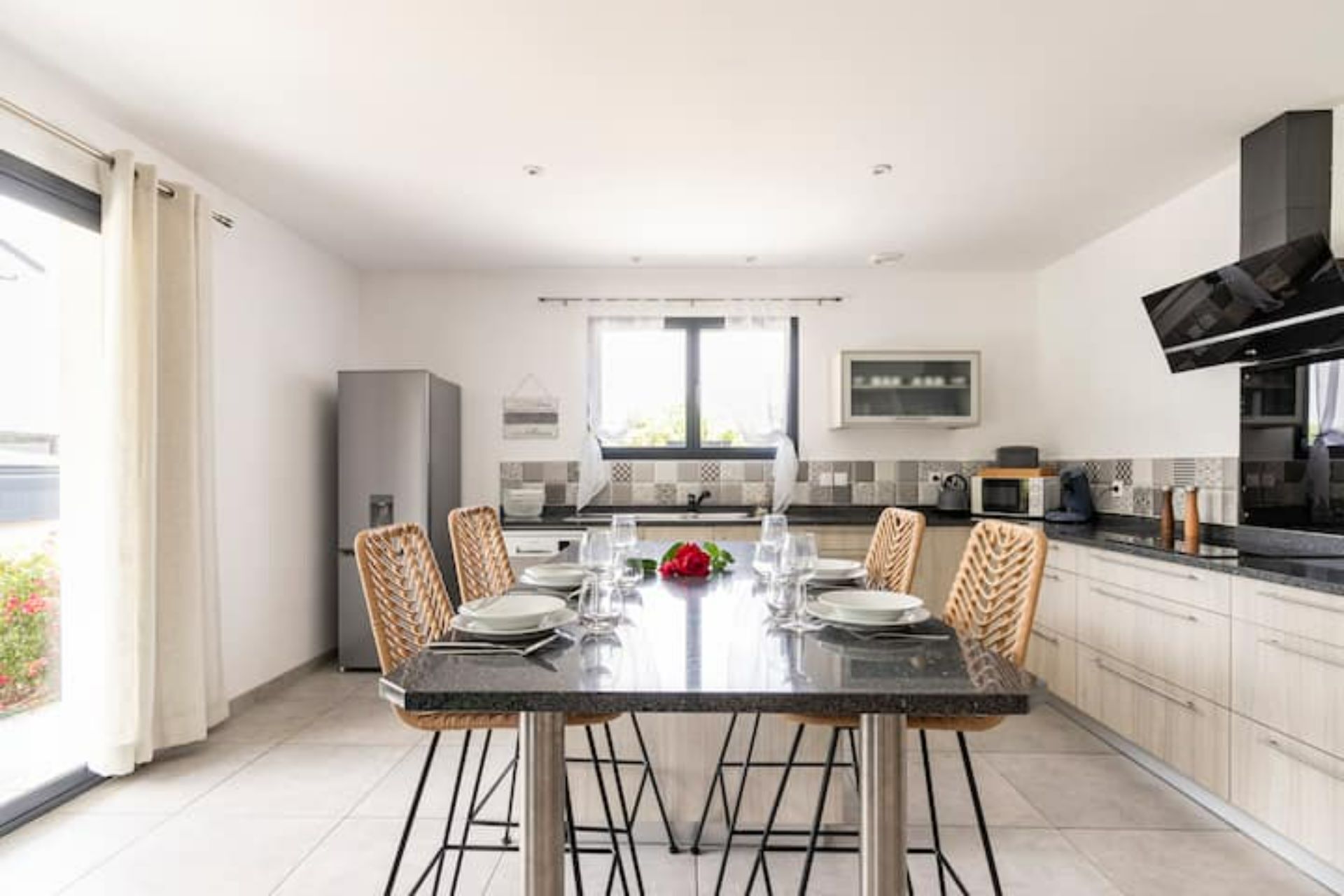 Une cuisine moderne avec une table à manger pour quatre personnes, agrémentée d’une rose rouge placée au centre.