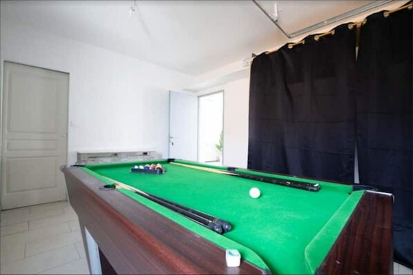 A pool table with balls and cues, a door, and a curtain.