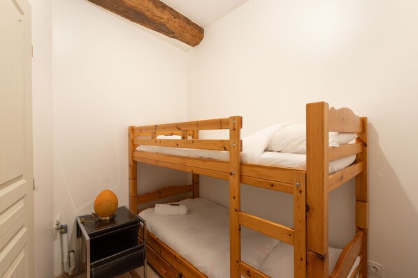 A bunk bed room with a wooden headboard, a small bedside table with a lamp, and a wall-mounted radiator.