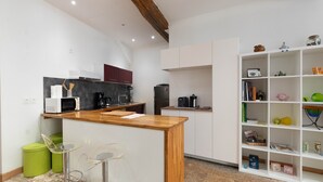 A modern kitchen with a wooden island, bar stools, and a white shelving unit with various items.