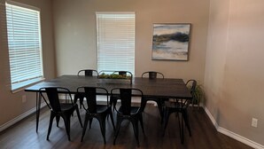 Une salle à manger avec une table en bois foncé, des chaises noires et un tableau accroché au mur.