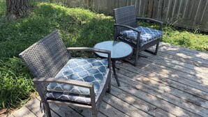 Une terrasse en bois avec des meubles en osier, notamment deux chaises et une petite table.