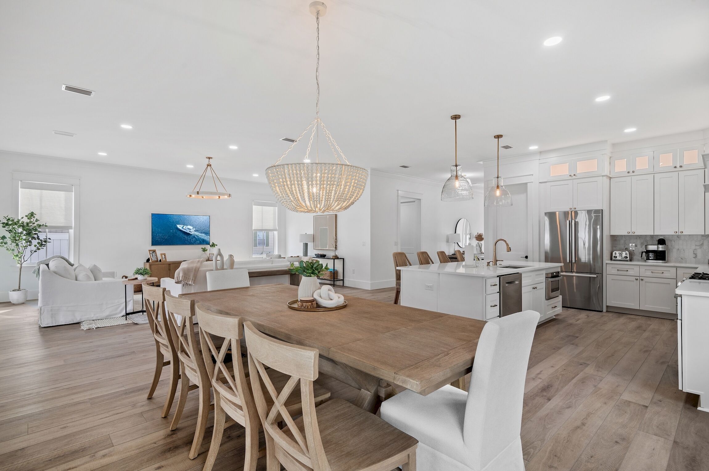 Une cuisine spacieuse avec des meubles blancs, une table à manger en bois et des luminaires suspendus.