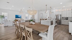 A spacious kitchen with white cabinetry, a wooden dining table, and pendant lighting. - Luxe 5BR with Pool, Hot Tub, Outdoor Kitchen, Bikes, Close to Beach & Seaside (Santa Rosa Beach)