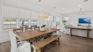 A spacious dining area with a wooden table and benches, large windows, and a chandelier. - Luxe 5BR with Pool, Hot Tub, Outdoor Kitchen, Bikes, Close to Beach & Seaside (Santa Rosa Beach)