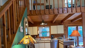 A cozy interior with a wooden staircase, a dining area with a table and chairs, a kitchen with a sink and counter, and a sofa with a blanket. - Cozy Mtn Log Cabin, wonderful views, 5 mins from Hayesville town sq, sleeps 8. (Hayesville)