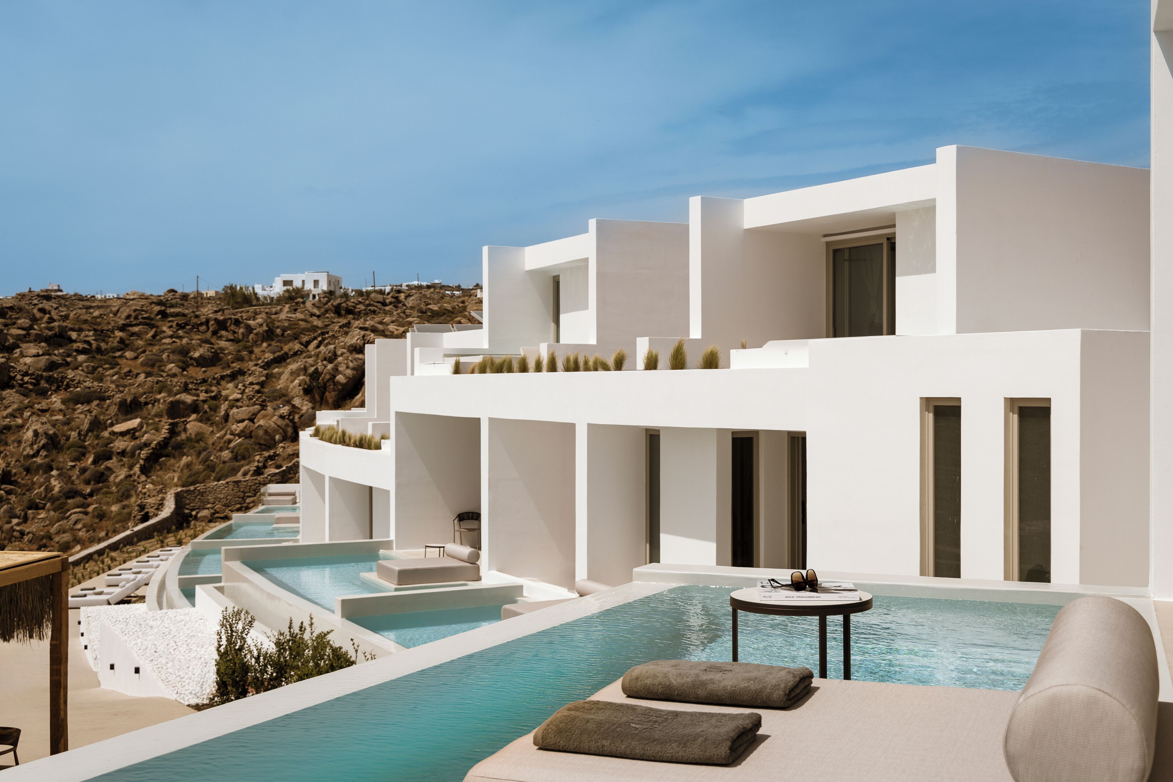 A modern hotel with a pool, white walls, and a view of a rocky hillside.