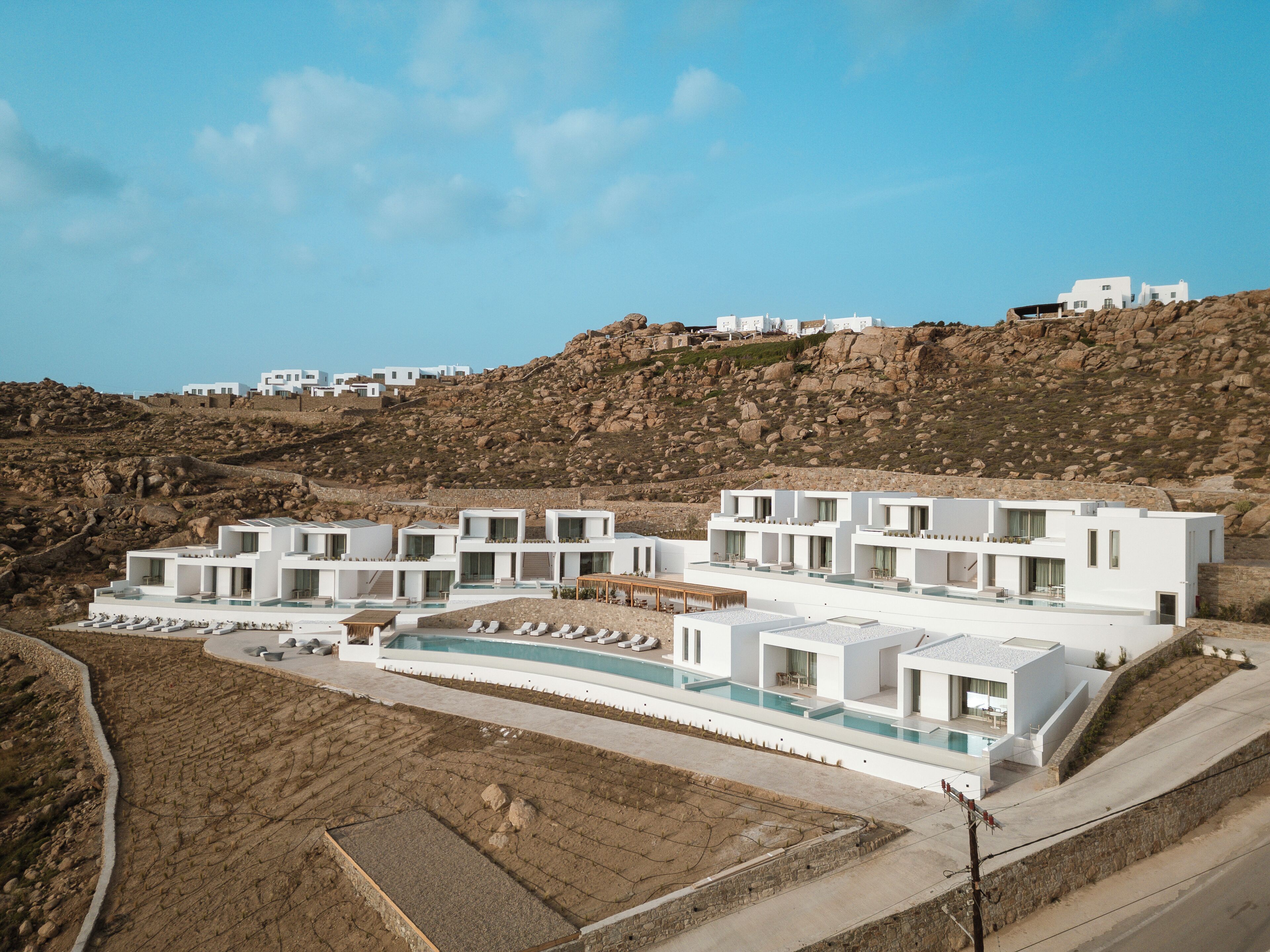 A modern white building with multiple balconies, a swimming pool, and a rocky hillside background.