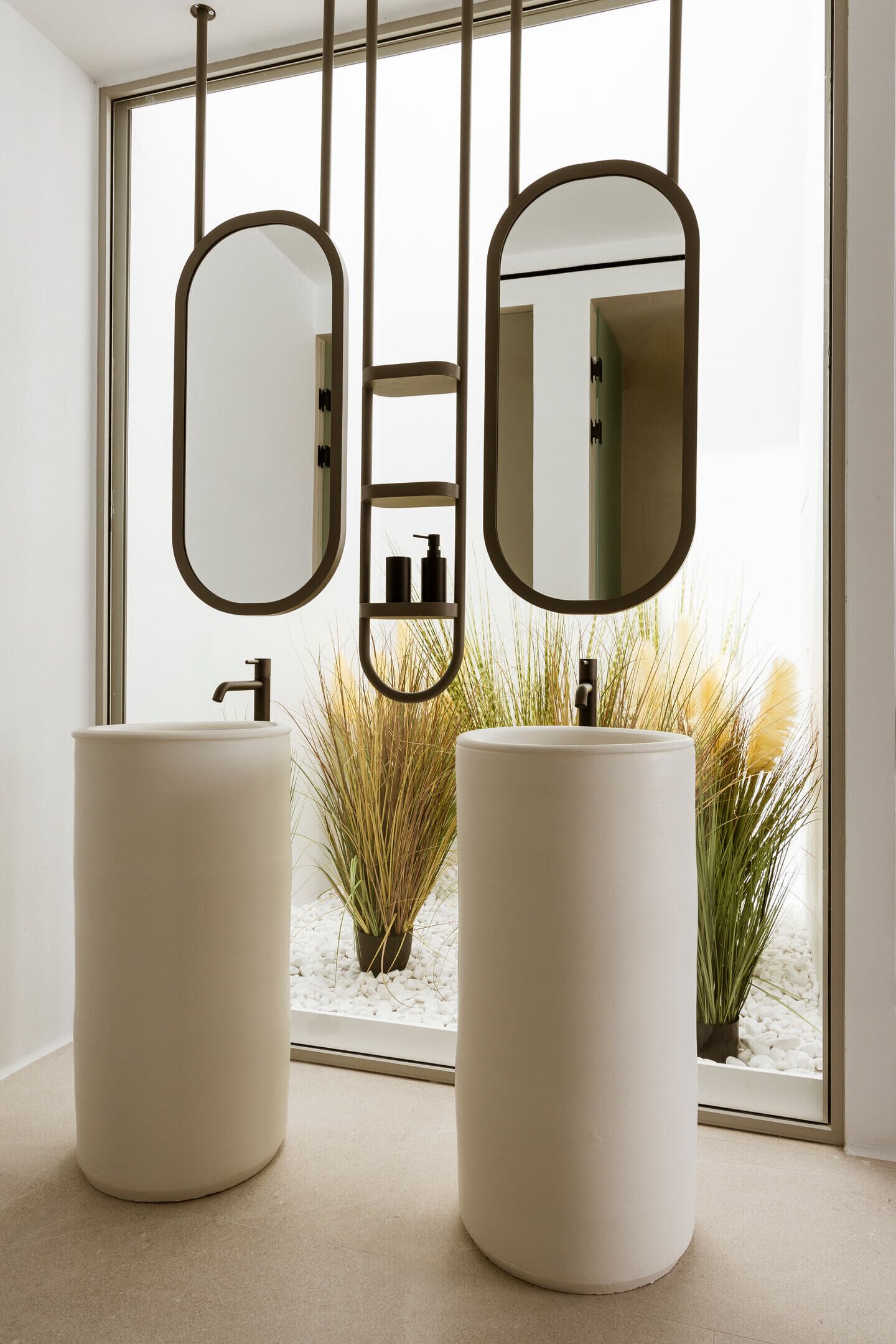 A bathroom with two round sinks, a mirror, and a window with a view of plants.